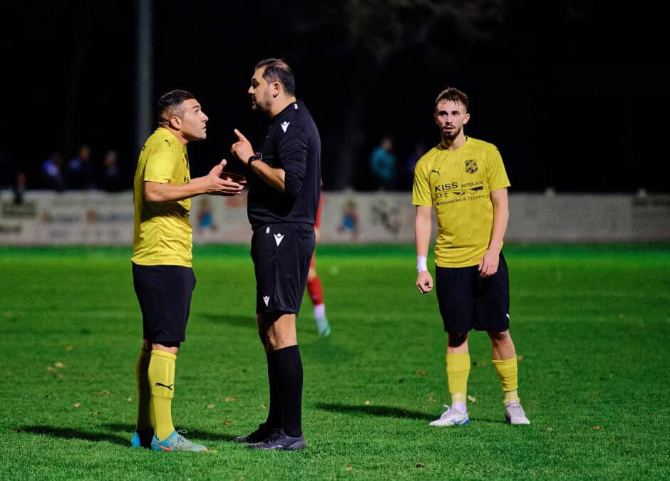 Referee Nevrez Cetiner warns Mustafa Atik: Mustafa Atik protests his innocence and slips away without a yellow card, after some grabs and trips, while teammate Ivan Ziga warily watches Subject: soccer;football;burgenland;kittsee;SC Kittsee;ASV Deutsch Jahrndorf