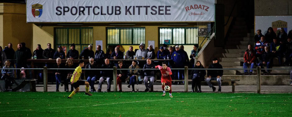 Fan Section: Maximilian Mikula knocks the ball into the center of the field in front of the main SC Kittsee fan section where Florian Gombay defends. Subject: soccer;football;burgenland;kittsee;SC Kittsee;ASV Deutsch Jahrndorf